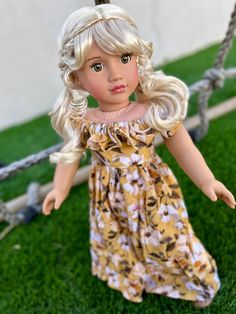 a doll with blonde hair wearing a yellow dress and holding onto a rope swing in the grass