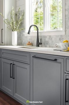 a kitchen with gray cabinets and white counter tops is pictured in this image, there are plants on the window sill