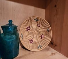 a basket sitting on top of a wooden shelf next to a blue vase and jar