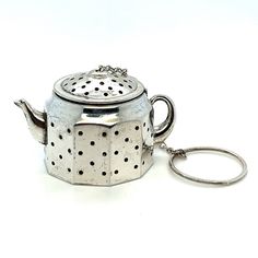 a teapot shaped keychain with holes on the front and sides, sitting on a white surface