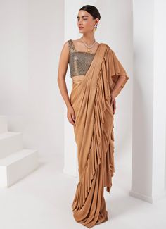 This elegant Gold Pre-Draped Lycra Saree Set, crafted from a luxurious blend of lycra and crepe, exudes timeless sophistication. The fluid draping of the gold saree, enhanced by the rich texture of the fabrics, makes it a standout choice for any special occasion. Paired with a striking grey blouse, intricately hand-embellished to add a touch of glamour, this ensemble is perfect for festive celebrations or sangeet ceremonies. Composition : Blouse - Crepe blend & Saree - Crushed Lycra Saree Care: Dry Clean Only and Vacuum Storage This product can be customized for sleeves, blouse length and neckline Delivery : 2-4 weeks as the product is hand crafted. Check Size Guide or choose MySize for free customisation (All Sizes above XL can be made at 15% additional cost) For more information and size Lycra Saree, Gold Saree, Vacuum Storage, Indian Wedding Wear, Grey Blouse, Sleeves Blouse, Western Design, Buy Gold, Blouse Length