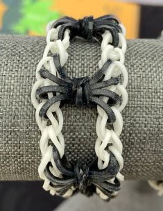 a black and white bracelet with an intricate knot on the clasp, sitting on top of a piece of fabric