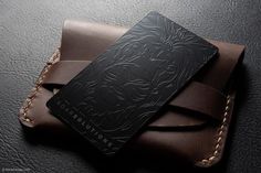 a black card case sitting on top of a brown leather wallet with stitching around the edges