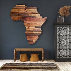 a wooden africa map hanging on the wall next to a table with vases and potted plants