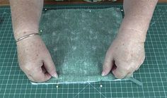 a person cutting fabric with scissors on top of a green mat and some other items