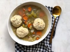 a bowl of soup with dumplings, carrots and celery next to a spoon