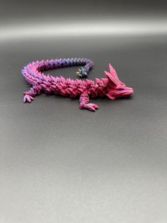 a pink and purple toy lizard sitting on top of a gray table next to a black object