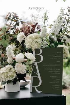 white flowers and greenery in vases on top of a table with a card