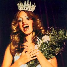 a woman wearing a tiara and holding flowers in front of her face with an open mouth