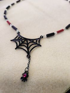 Just in time for Halloween, this spider web necklace is sure to delight. Fully hand made links make this a one-of-a-kind piece. The links feature black and red glass beads. This necklace measures 16.5 inches in total length. The handmade links are crafted from silver filled wire. The closure is a sterling silver lobster claw clasp. It is a very lightweight piece, made from tarnish resistant silver wire, so it is comfortable for all day wear and will last for years to come. And to top it all off, the web is complete with a hanging spider sporting a pink jewel. Gothic Black Necklace With Lobster Clasp, Black Gothic Necklace With Lobster Clasp, Black Halloween Necklace With Lobster Clasp, Adjustable Black Vampire Necklace, Adjustable Black Vampire Style Necklaces, Handmade Black Vampire Necklace, Handmade Red Necklaces For Halloween, Handmade Black Witchy Necklace, Handmade Red Halloween Necklaces