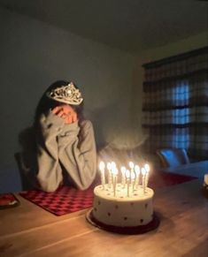 a woman sitting at a table in front of a cake with lit candles on it