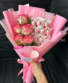 a hand holding a bouquet of pink roses with candy bars in the back and on the side