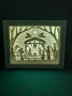 an illuminated nativity scene is displayed in a shadow box on a green tablecloth