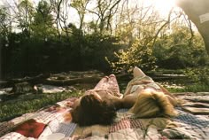 two people laying on a blanket in the woods