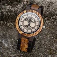 Experience the merging of art, nature, and timekeeping with our mesmerizing Tree of Life Yggdrasil Wooden Watch.  This exquisite timepiece showcases a stunning Yggdrasil tree on its wooden face, capturing the essence of strength and wisdom. The watch's wooden construction, combined with its intricate design, creates a visually captivating accessory that is sure to make a statement.  With its precise Japanese quartz movement and adjustable band, this watch offers both style and functionality.  Each watch is carefully made with utmost attention to detail, resulting in a unique and high quality piece that is as exceptional as the legend it represents.  Take a piece of ancient mythology with you wherever you go with our Tree of Life Yggdrasil Wooden Watch. Unique, high-quality wooden watch, en Analog Jewelry And Watches With Round Dial For Gifts, Brown Analog Display Watch As Gift, Engraved Brown Watches For Gift, Engraved Brown Watches As Gift, Engraved Brown Watches For Gifts, Brown Engraved Watch For Gift, Brown Engraved Watches As Gifts, Handmade Black Watch As A Gift, Handmade Black Watches As A Gift