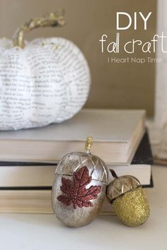 two small pumpkins sitting on top of books next to a white pumpkin with leaves painted on it