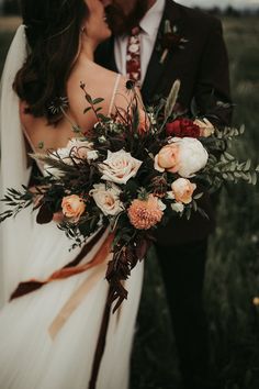 a bride and groom kissing in a field with flowers on their wedding day at sunset