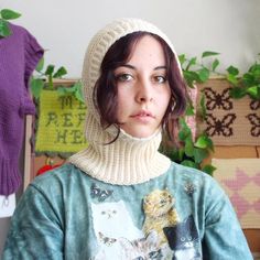 a woman wearing a knitted hat and sweater with cats on it, standing in front of plants