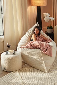 a woman laying in a bean bag chair on top of a bed next to a window