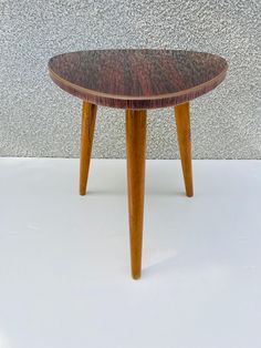 a small wooden table sitting on top of a white floor next to a gray wall