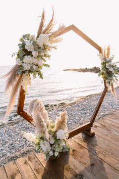 an arch decorated with flowers and feathers on the beach