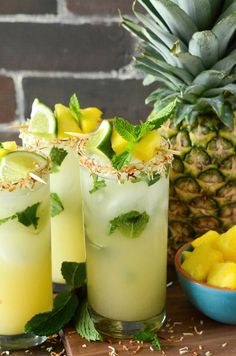 two glasses filled with lemonade, lime and mint garnish next to pineapples