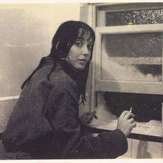 a woman sitting in front of a window writing on a piece of paper