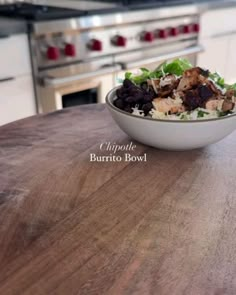 a bowl filled with food sitting on top of a wooden table next to an oven