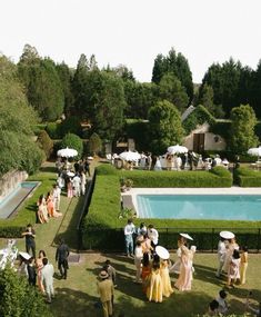 a group of people standing in front of a pool surrounded by lush green grass and trees