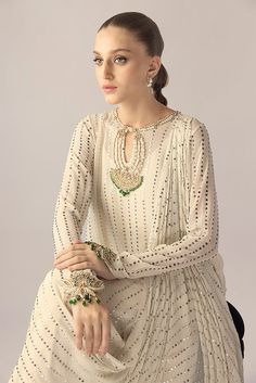 An ivory georgette long shirt with a draped dupatta is handworked with delicate kamdani. The sleeves and neckline are detailed with jewelled floral motifs. An elegant ensemble for any formal event or soiree. Elegant Georgette Palazzo Set For Reception, Elegant Floor-length Palazzo Set For Reception, Hand Embellished Palazzo Set For Party, Elegant Palazzo Set For Reception With Traditional Drape, Elegant Resham Embroidery Palazzo Set For Reception, Hand Embellished Georgette Palazzo Set For Reception, Elegant Embellished Palazzo Set For Reception, Designer Hand Embellished Georgette Sharara, Georgette Palazzo Set For Reception