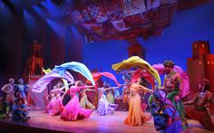 a group of people standing on top of a stage wearing colorful outfits and holding umbrellas