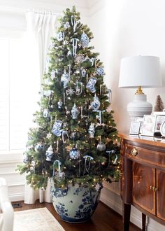 a decorated christmas tree in a blue and white pot on a wooden floor next to a window