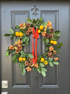 a wreath with oranges and pine cones hanging on a door