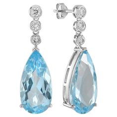 The handcrafted vintage style Blue Topaz and Diamond Drop Earrings feature a pair of pear-shaped topaz in a sky blue hue set in a fine claw setting. These settings are elegantly hanging from diamond set stud fitting. The earrings are incredibly comfortable to wear because the back helps distribute the weight of the earrings while lifting the post of earrings on your earlobes. Earrings Information Metal: 14K White Gold Width: 14 mm. Length: 21 mm. Weight: 6.00 g. (approx. in total) Backing: Push Back Drop Gemstones Type: Blue Topaz Shape: Pear Size: 20 x 10 mm. Number: 2 Weight: 30 Carat (approx. total weight) Accent Gemstones Type: Diamond Shape: Round Average Color: H Average Clarity: SI Size: 2.2 - 3 mm. Number: 6 Weight: 0.40 Carat (approx. total weight) These earrings will be made to y Art Deco Drop Earrings, Earring Box, Halo Earrings, Claw Setting, Blue Topaz Stone, A Sky, Tiny Diamond, Sky Blue Topaz, Diamond Drop Earrings