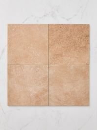 a square tile with four squares on it in light brown and white marble, set against a wall