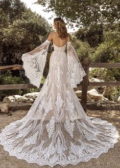 a woman in a white wedding dress standing on a wooden fence with her back to the camera