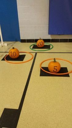 three pumpkins with numbers on them sitting in an indoor gym area, surrounded by hula hoopes