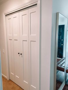 a white closet with mirrored doors in the corner next to a bench and mirror on the wall