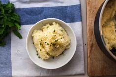 mashed potatoes in a white bowl on a wooden cutting board next to a blue and white towel