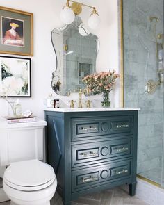 a white toilet sitting next to a blue dresser in a bathroom under a large mirror