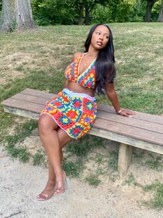 a woman sitting on a wooden bench in a colorful dress with trees in the background