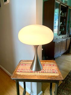 a lamp sitting on top of a wooden table next to a wall with a rug