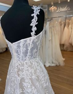 the back of a white wedding dress on display in a bridal shop with other dresses