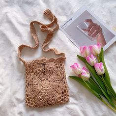 a crocheted purse next to flowers on a white sheet with a book and photo