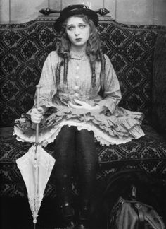 an old black and white photo of a woman sitting on a couch wearing a hat