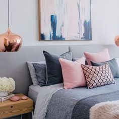 a bedroom with pink and grey decor on the walls, gray bedding, white pillows, and gold accents