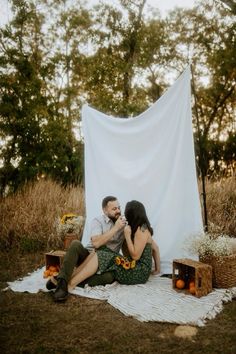 a man and woman sitting on the ground in front of a white tarp with pumpkins