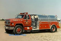 an old fire truck is parked in the sand near some buildings and water tanks on it's flatbed