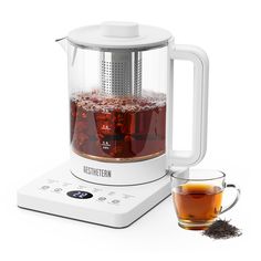 a glass tea pot filled with liquid next to a cup of tea