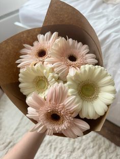 a bouquet of white and pink flowers in someone's hand on a bed sheet